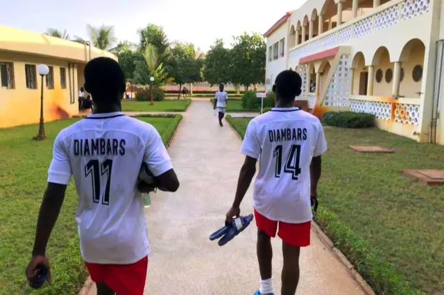 Deux joueurs vétus de maillot blanc, short rouges marchent en direction du terrain. 