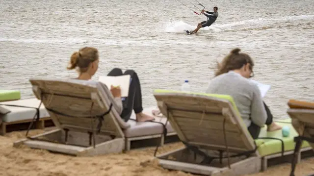 Deux vacanciers profitant des plages du Sahara occidental sous le soleil, avec un pratiquant de kitesurf dans les vagues