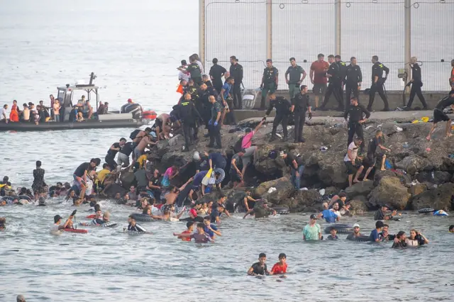 Migrants traversant la frontière vers Ceuta, illustrant les tensions géopolitiques en Méditerranée.